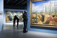 Visitors stood in IWM London's Blavatnik Art, Film and Photography galleries, admiring artworks, including 'Oppy Wood, 1917, Evening' by John Nash.