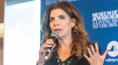 A photo of Menin speaking into a mic.