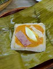 filipino tamales topped with flaked chicken and and hard boiled eggs on a serving plate.