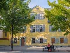 Auf einer Bank vor Schillers Wohnhaus sitzen Menschen.