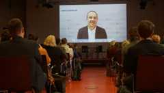 Auf die Bühnenrückseite ist groß ein Video projiziert in dem der sächsische Staatsminister für Landwirtschaft die Teilnehmenden begrüßt