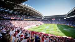 Die ausverkaufte Red Bull Arena, fotografiert aus dem RB-Fanblock. Im Vordergrund halten Fans ihre Schals nach oben.