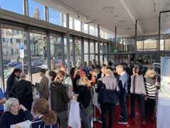 Mehrere Menschen stehen in einem hellen Raum mit großen Fenstern und unterhalten sich.