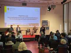 Matthias Kaufmann steht vor der Bühne und spricht mit Mikrofon in der Hand zum Publikum