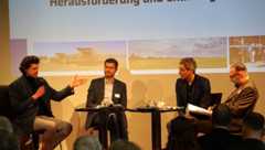 Vier Männer sprechen auf einem Podium miteinander. Im Hintergrund Landwirtschaftsbilder.