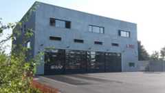 Die Gebäudeansicht zeigt die komplette Gebäudeseite mit den beiden großen Toren in die Fahrzeuggaragen und einen kleinen Teil das asphaltierten Platzes davor.