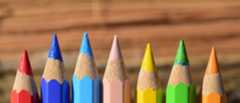 Man sieht sieben Buntstifte in verschiedenen Farben in einer Reihe.