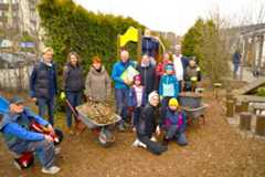 Eine Gruppe von Erwachsenen und Kindern steht mit Schubkarren auf einem Spielplatz
