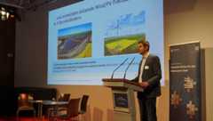 Martin Faßhauer von den Stadtwerken Leipzig spricht zum Thema erneuerbare Energieerzeugung in Leipzig. Dabei steht er am Rednerpult auf der Bühne und im Hintergrund ist seine Präsentation zu sehen.