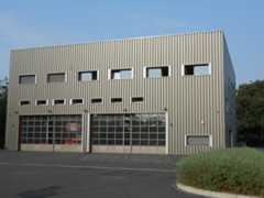 Die Gebäudeansicht zeigt die komplette Gebäudeseite mit den beiden großen Toren in die Fahrzeuggaragen und einen kleinen Teil das asphaltierten Platzes davor.