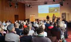 Ein Mann und eine Frau unterhalten sich auf der Bühne. Davor sitzt das Publikum und hört zu.