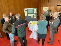 Menschen unterhalten sich an Stehtischen und vor einer Pinwand