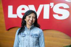 A portrait of Levi Strauss Foundation Executive Director Fatima Angeles smiling in front of a red Levi's® sign. She wears a blue Levi's® button up top.