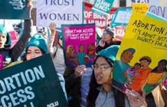 People gather holding signs advocating for reproductive rights and abortion access.