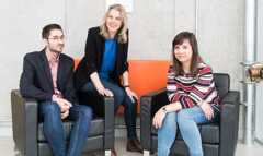 Two women and one man sitting on sofas looking at the camera
