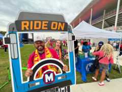 Man posing playfully with a "RIDE ON" photo prop of a MetroBus windshield as if he were the bus operator.