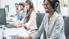 Customer service agents sitting with headsets at laptops smiling.