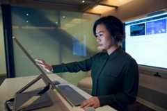 Side profile of a woman wearing a dark shirt in a dim office scrolling or working on a Microsoft Surface Studio.