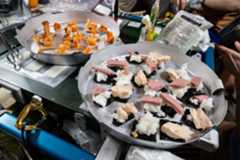 Two metal trays of food are attached to a surface by Velcro strips. The tray in the foreground has sushi on it, while the tray in the back has shrimp cocktail on crackers.