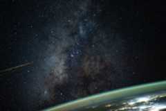 The Milky Way galaxy appears above Earth's greenish atmospheric glow. The galaxy's dust and stars can be seen against the darkness of space.