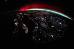 A green and red aurora streams across Earth’s horizon above the city lights of Europe.