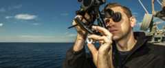 A United States Navy Quartermaster uses a sextant to the measure the angle of the sun on the USS San Jacinto cruiser.
