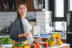 Pregnant lady in a kitchen with an array of fresh vegetables on the counter