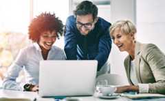 A group of marketers laughing and viewing untapped market opportunities on a laptop provided by Nielsen's streaming measurement solution.