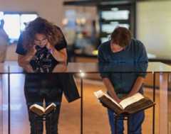 אנשים מסתכלים על ספרים על סטנדים המוצגים בתערוכת הקבע