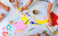 Detail image from above a table, with children's hands doing various arts and crafts.