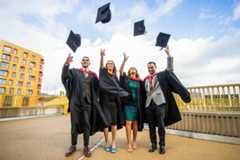 Two female and two male graduates in caps and gowns throwing their mortar boards up in the air.