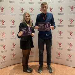 Students at Skills Competitions Wales Celebration event in front of advertising board with the certificates.