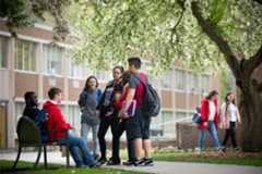 Students in a spring quad talking in a circle. Two students are sitting on a bench.
