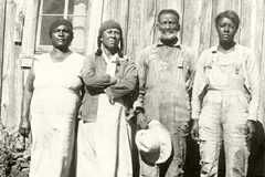 An older man stands ouside a wooden structure with three women