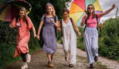 Four woman walk down a country path holding colourful umbrellas.