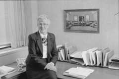 Loretta Ford, former School of Nursing dean, is depicted in a suit and tie, seated at a desk in a professional setting.