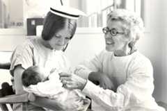 A nurse in uniform cradles a baby, symbolizing care and compassion, inspired by Loretta Ford's legacy in nursing education.