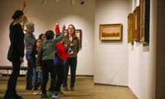 A group of schoolchildren with their hands raised and their Expanded Learrning Collaboration instructors at the Memorial Art Gallery.