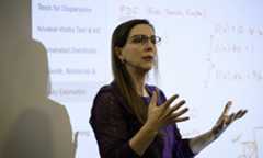 Katherine Grzesik in a classroom teaching and gesturing at a screen with equations.