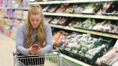 a woman in a supermarket with a shopping trolley using her phone