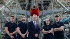 Young apprentices pose under the tail of an airplane with Minister James Lawless in the centre.