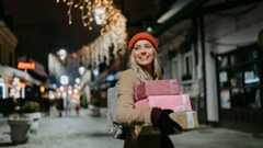 Photo of a young woman walking through the town and carrying Christmas presents.