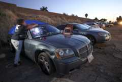 While parked in a row of cars belonging to  homeless people, a person puts a tarp over her car as she prepares to spend the night in it at a safe lot operated by Dreams for Change in San Diego, California. (Hayne Palmour IV / U-T File)