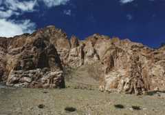 A reddish rocky ridge rises up beneath a blue sky with white clouds.