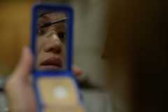 Part of a face is reflected in a handheld compact mirror as a person applies mascara.