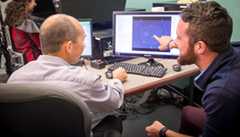 Two people looking at a computer and talking to each other.