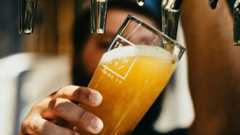 person holding clear drinking glass, filling it with yellow brown liquid