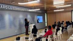 A classroom with about a dozen students seated in white chairs, facijng a speaker at a white podium in front of a sign reading Community Engagement Center.