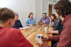 Seven STF team members sitting around a wooden table in the office kitchen, smiling and laughing.