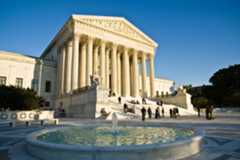 The Supreme Court Building facade and front plaza with a fountain in the foreground. Several visitorsstand on the plaza and on the building�s front steps.
